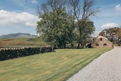 a stone house in a field with a stone fence at North Lakes - The Fold Holiday Cottage in Penrith
