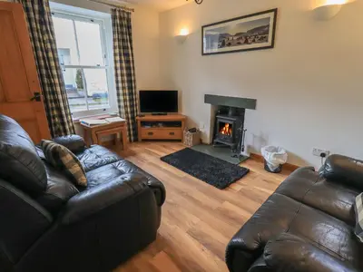 a living room with a leather couch and a fireplace at Capella Cottage in Keswick