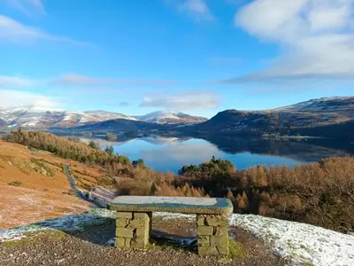 a stone bench sitting on top of a hill overlooking a lake at Catbells Sunrise Cottage Borrowdale Lake District in Keswick