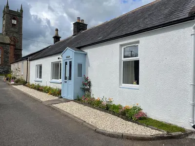 a white house with a blue door on a street at Glencairn Cottage in Moffat