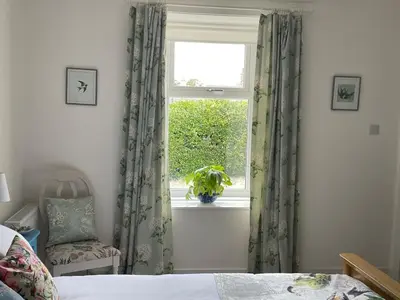 a bedroom with a window with a plant and a chair at Glencairn Cottage in Moffat