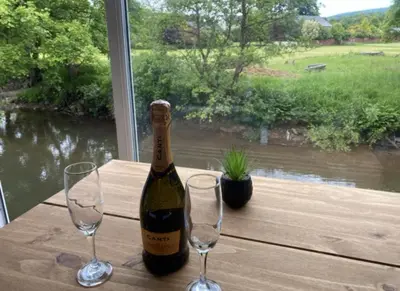 a bottle of wine sitting on a table with two glasses at Riverbank Cottage River Ehan Double Balcony in Egremont