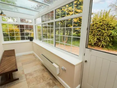 a conservatory with windows and a bench and a table at Kirkland Howe Cottage in Frizington