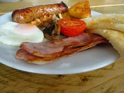 a plate of breakfast food with bacon eggs sausage and a tomato at Lake View Country House and Self-catering Apartments in Grasmere