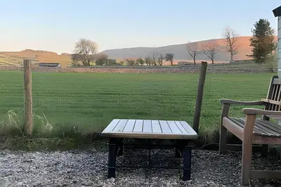 a picnic table and a bench in front of a field at Cozy Cottage in Caldbeck in Caldbeck