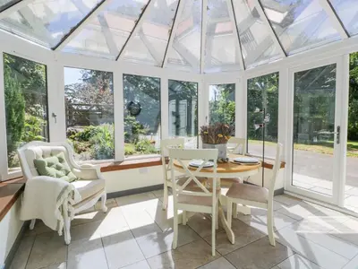 a conservatory with a table and chairs and windows at Nithbank Cottage in Thornhill