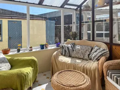 a conservatory with a couch and chairs and windows at Midtown House in Aspatria