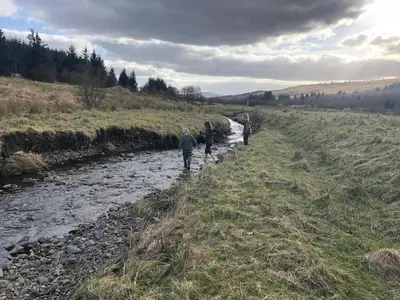 a group of people walking across a river at Corlae Cottage, mountain and forest views in Carsphairn
