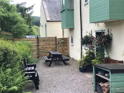 a picnic table and benches in front of a house at Corlae Cottage, mountain and forest views in Carsphairn