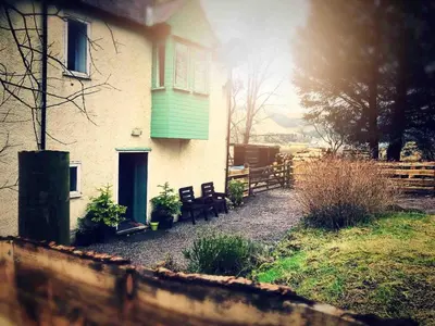 a house with a green door and benches in front of it at Corlae Cottage, mountain and forest views in Carsphairn
