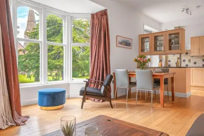 a living room with a table and chairs and a large window at Chaucer Apartment in Keswick
