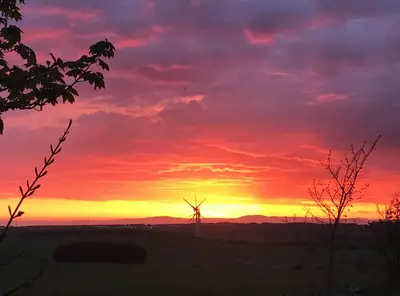 a sunset with a windmill in a field at The MireHouse - Georgian rural retreat in Ullock