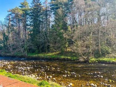 a river with rocks and trees in the background at Rubby Banks Retreat in Cockermouth