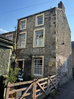 an old stone house with windows and a wooden fence at Sycamore Cottage - Lake District Hiking & Rivers in Cockermouth
