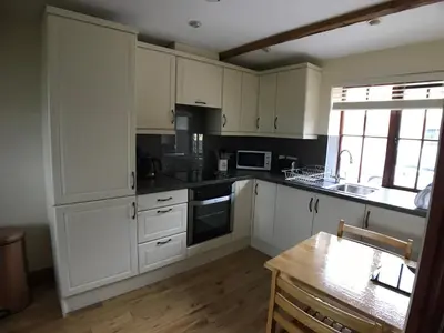 a kitchen with white cabinets and a wooden table at Castlehead Cottage in Keswick