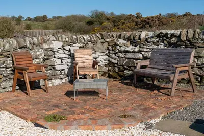 three wooden chairs and a bench on a brick patio at The Larroch Byre in Monreith