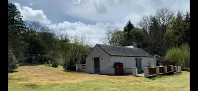 a small white building in a field with a fence at Whitestone Cottage in Turnberry