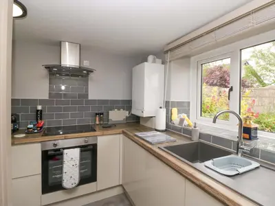 a kitchen with white cabinets and a sink and a window at Yeat Stoup Cottage in Cockermouth