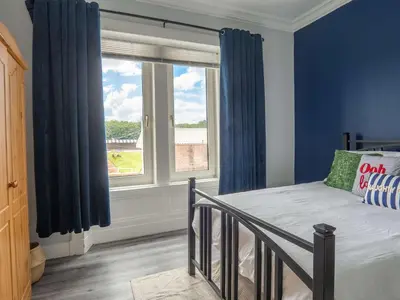 a bedroom with a bed with blue curtains and a window at Pitchside Escape in Ayr