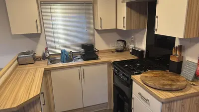 a kitchen with white cabinets and a stove top oven at Tattershall caravan with private hot tub in Moffat