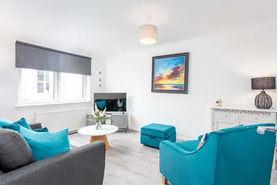 a living room with blue furniture and a tv at Albyn Retreat - Donnini Apartments in Prestwick