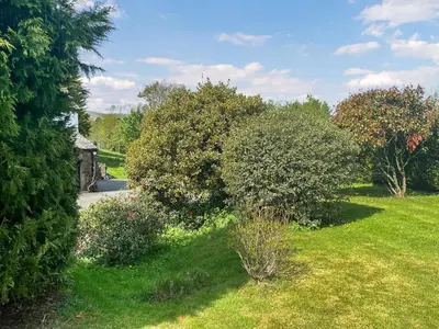 a garden with bushes and trees and a road at Gillhead Farm Cottage in Troutbeck