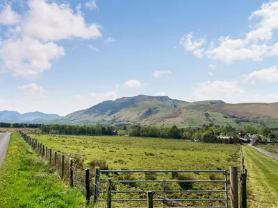 a fence in a field with mountains in the background at Gillhead Farm Cottage in Troutbeck