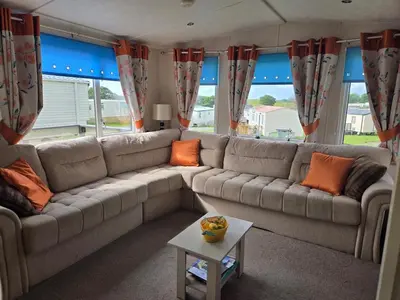 a living room with a large couch with orange pillows at Lovely Caravan number 96 at Three Lochs Holiday Park in Kirkcowan