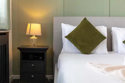 a bed with white pillows and a lamp on a night stand at No15 Ellis House - Donnini Apartments in Kilmarnock