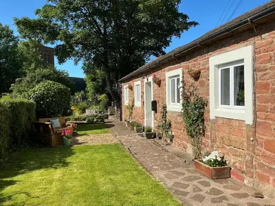 a brick house with a grass yard in front of it at Abbey Cottage in St Bees