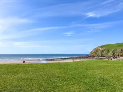 a beach with a green field and the ocean at Abbey Cottage in St Bees
