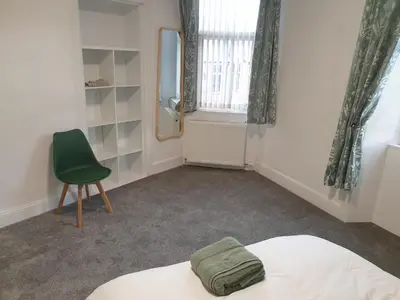 a bedroom with a bed and a chair and a mirror at Modern Two-Bedroom Apartment Near River with Free Parking & WiFi in Dumfries