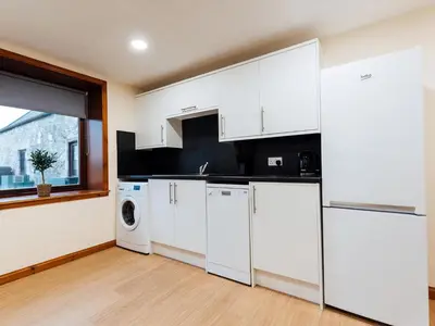 a kitchen with white cabinets and a washer and dryer at The Barn in Girthon