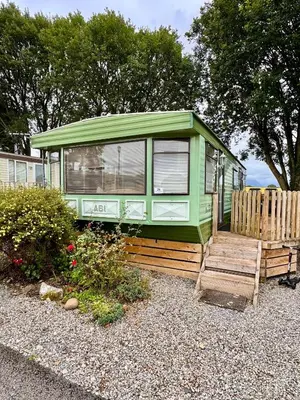 a green house with a wooden porch and a fence at No 26 Mountain View in Cockermouth