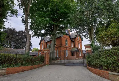 a large brick house with a fence and trees at 2 On The Green in Moffat