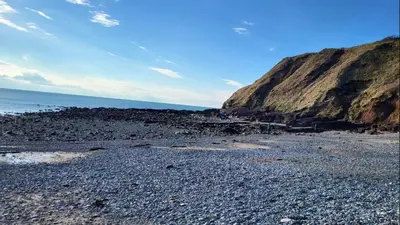 a rocky beach with a large cliff next to the ocean at Coach House Apartment - Sleeps 2 in Whitehaven
