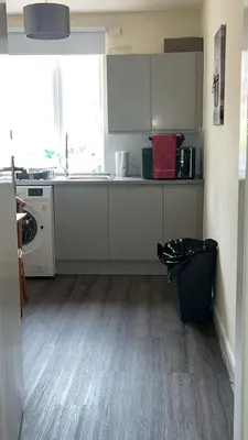 a kitchen with white cabinets and a black trash can at QueensBerry accommodation in Annan
