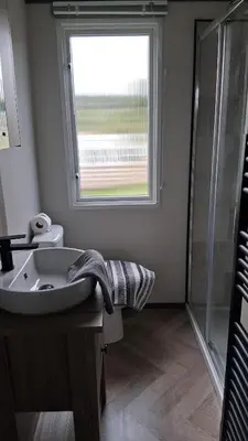a bathroom with a sink and a window and a shower at Three Lochs Holiday Park- Lochwood Caravan in Newton Stewart