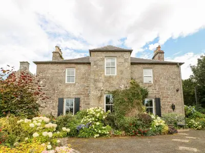 an old stone house with flowers in front of it at Balsaggart Farm in Maybole