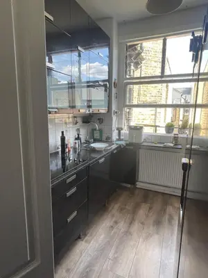 a kitchen with black cabinets and a wooden floor at Bright peaceful room 4th floor in front Battersea park in Moffat