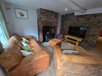 a living room with two leather couches and a fireplace at Lakes Cottage Beckermet in Beckermet