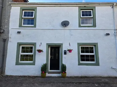 a white house with green windows and a door at Lakes Cottage Beckermet in Beckermet