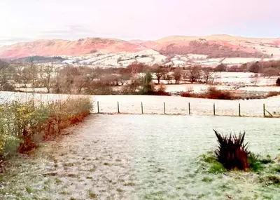 a field covered in snow with a fence and mountains at Lorton View, nestles on the fellside with walks from the door close to Lorton in Lorton