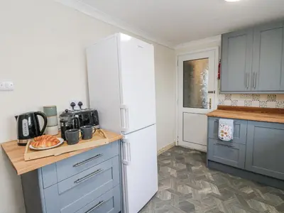 a kitchen with a white refrigerator and blue cabinets at Daisy Cottage in Wigton