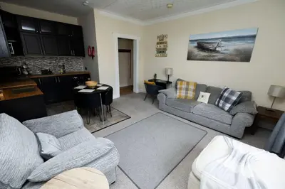 a living room with a couch and a kitchen at Troon - Coastal Getaway in Troon