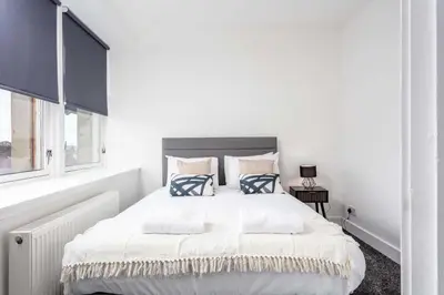 a white bedroom with a large bed with blue pillows at Weaver Suite - Donnini Apartments in Ayr