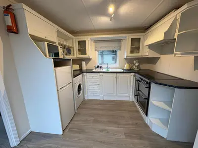 a kitchen with white cabinets and a white refrigerator at Cosy Caravan by the sea in Cairnryan