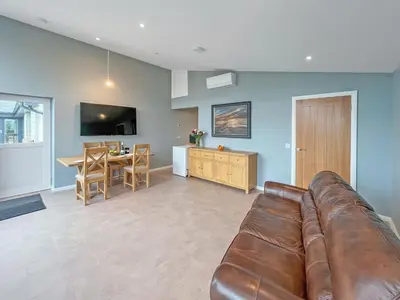 a living room with a leather couch and a dining room at Grey Rocks Apartment in Kippford