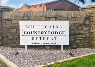 a white sign in front of a brick wall at Whitecairn Holiday Park in Glenluce