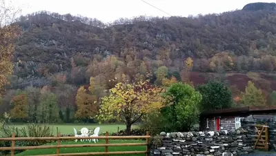 two chairs and a stone wall in front of a mountain at Mountain Lodge, Lake View, National Park in Borrowdale Valley